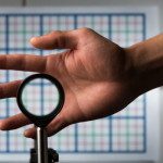 A multidirectional `perfect paraxial' cloak using 4 lenses. For a continuous range of viewing angles, the hand remains cloaked, and the grids seen through the device match the background on the wall (about 2 m away), in color, spacing, shifts, and magnification. The edges of the optics can be seen since this is a small-angle ('paraxial') cloak, but this can be reduced by using large optics and for distant viewing; also the center of the device must not be blocked. // an optical cloaking configuration designed by University of Rochester professor of physics John C. Howell and Ph.D. student Joseph Choi is pictured in Bausch & Lomb Hall September 11, 2014. // photo by J. Adam Fenster / University of Rochester